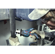 Artisan coupant un tuyau sombre avec une scie sabre sans fil Bosch Professional dans une zone de travail avec des tuyaux métalliques argentés.