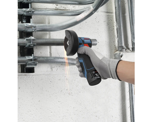 Meuleuse angulaire sans fil 12 Volt Bosch Professional coupant un tuyau métallique sur un mur avec des étincelles.