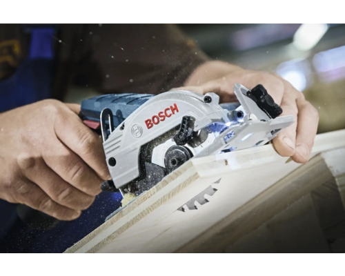 Eine Person schneidet mit einer Bosch Kreissäge ein Holzbrett, wobei Sägespäne entstehen.