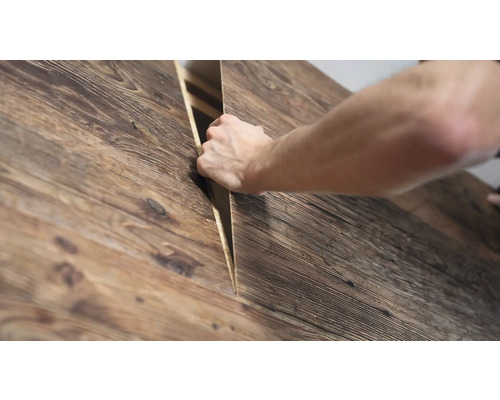 Une main soulève un panneau en bois à l'aspect rustique et à la structure veinée.