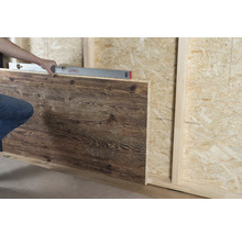 Une personne aligne un panneau mural imitation bois sur un mur en bois avec un niveau à bulle.