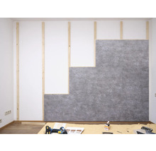 Montage grauer Wandpaneele in Betonoptik auf einer Holzlatten-Unterkonstruktion an einer weißen Wand im Innenraum.