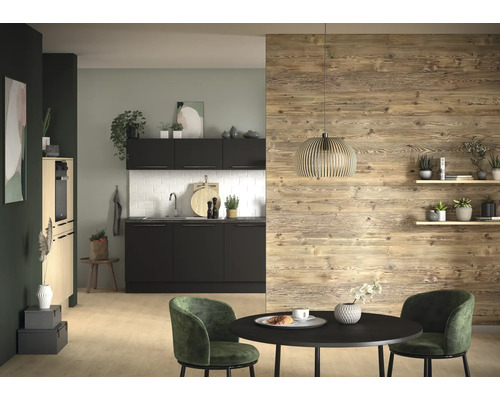 Cuisine moderne avec armoires noires, crédence en carreaux blancs et mur en bois. Devant se trouve une table ronde noire et des chaises vertes.