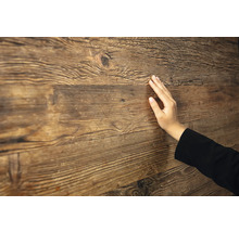 Main touchant une surface en bois rustique avec un grain et une texture prononcés.