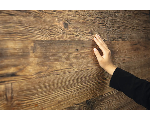Main touchant une surface en bois rustique avec un grain et une texture prononcés.