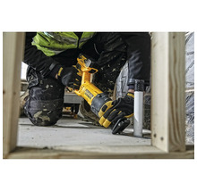 Artisan utilisant une scie sabre sans fil DeWalt pour couper un tuyau en plastique près d'un cadre en bois sur un chantier lumineux.