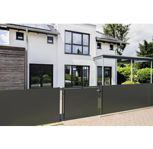 Maison moderne blanche avec fenêtres sombres et une clôture pare-vue anthracite incluant un portillon devant une zone pavée.