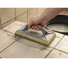 Taloche éponge utilisée pour nettoyer des carreaux fraîchement jointoyés. Une main guide l'outil sur les carreaux mouillés.