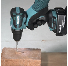 Perceuse-visseuse à percussion sans fil Makita 18 Volts avec foret à béton perçant une brique.