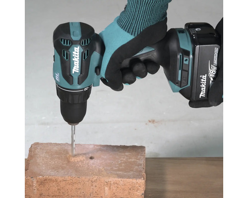 Perceuse-visseuse à percussion sans fil Makita 18 Volts avec foret à béton perçant une brique.