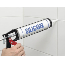 Application de silicone avec un pistolet à cartouche sur un joint de carrelage.