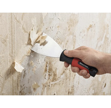 Spatule de peintre Rautner enlevant du vieux papier peint d un mur. Spatule avec poignée ergonomique et lame en métal.