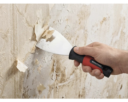 Spatule de peintre Rautner enlevant du vieux papier peint d un mur. Spatule avec poignée ergonomique et lame en métal.