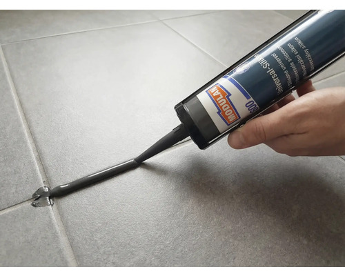 Modulan 600 Universal-Silikon wird mit einer Kartusche in eine Fliesenfuge auf grauen Bodenfliesen aufgetragen.