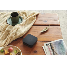 Aqara Smart Home Hub M2 sur une table en bois a cote d une tasse de cafe sur une couverture en tricot, une assiette de fruits et un magazine.