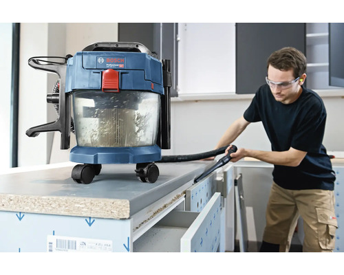 Aspirateur eau et poussière sans fil Bosch utilisé pour nettoyer un établi dans un atelier lumineux.