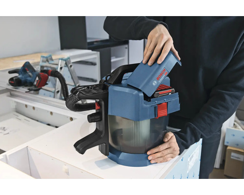 Une personne insère une batterie de 18 Volts dans un aspirateur sans fil Bosch Professional GAS 18 Volt-1 dans un atelier.