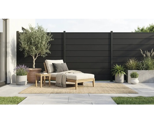 Clôture brise-vue moderne à lamelles anthracite sur une terrasse avec chaise longue en bois et diverses plantes en pot.