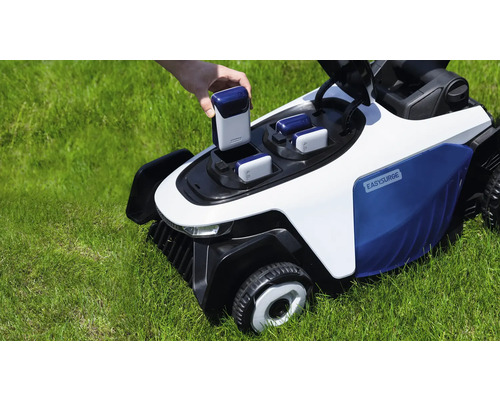 Une main insère une batterie dans une tondeuse robot Easysurge blanche et bleue sur une pelouse verte.