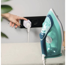 Une main appuie sur le bouton de la prise intelligente blanche reliee au fer a repasser dans la prise murale noire.