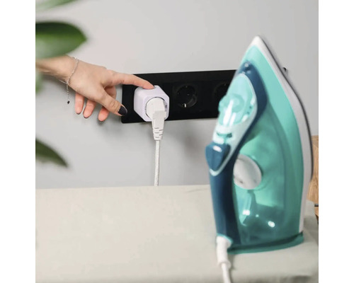 Une main appuie sur le bouton de la prise intelligente blanche reliee au fer a repasser dans la prise murale noire.