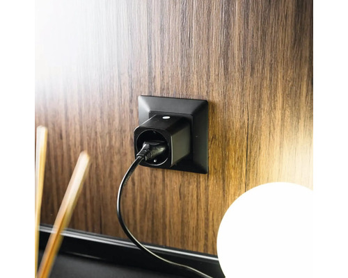 Prise connectée noire insérée dans une prise murale sur un panneau en bois avec un câble d'alimentation branché.
