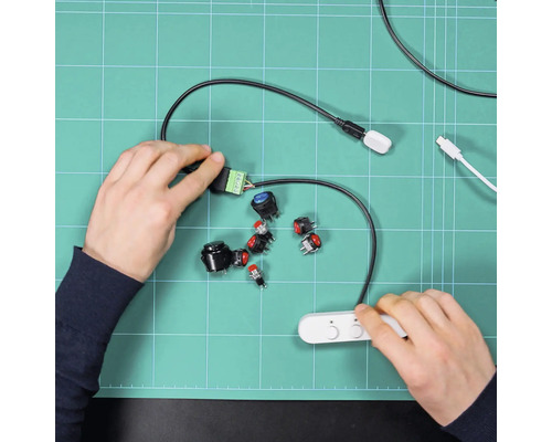 Des mains assemblent différents boutons-poussoirs et composants électroniques sur un tapis de découpe vert pour un projet de bricolage.