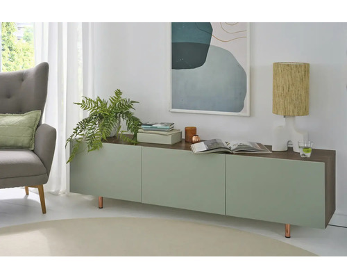 Helles, modern ageriichtent Wunnzëmmer mat engem Sideboard a Gréng an Holzoptik, engem groe Fotell, enger Zëmmerplanz an enger Tischluucht.