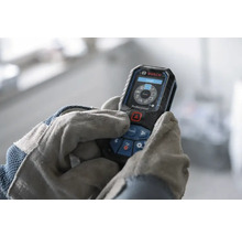 Bosch Professional Laser-Entfernungsmesser bedient von Händen in Arbeitshandschuhen, digitales Display mit Messfunktionen.