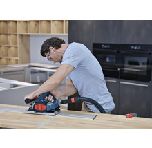 Mann nutzt eine Handkreissäge mit Führungsschiene und Staubabsaugung auf einer Holzoberfläche in einer Küche.