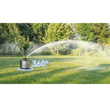Ein AL-KO Rasensprenger auf einer grünen Wiese in einem hellen Garten bewässert die Fläche in einem 360 Grad Winkel.