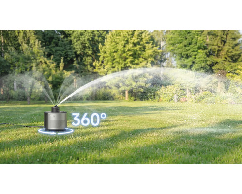 Ein AL-KO Rasensprenger auf einer grünen Wiese in einem hellen Garten bewässert die Fläche in einem 360 Grad Winkel.