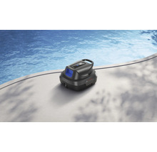 Ein schwarzer Poolroboter steht auf einem hellen Beckenrand neben einem Schwimmbecken mit blauem Wasser.