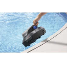 Eine Hand hält einen grauen Poolroboter am Griff über den Rand eines Schwimmbeckens mit klarem blauem Wasser.