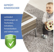 Weißer Kantenschutz an einem Holztisch, daneben ein spielendes Kind auf einem Teppich, Siegel geprüft kindersicher.