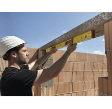 Ouvrier utilisant un niveau à bulle pour aligner un linteau en béton au-dessus d'un mur en briques sur un chantier.