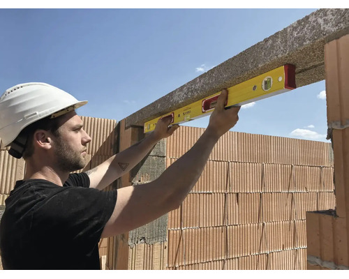 Ouvrier utilisant un niveau à bulle pour aligner un linteau en béton au-dessus d'un mur en briques sur un chantier.