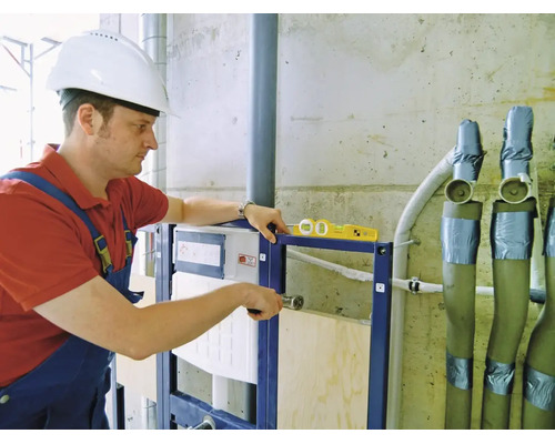 Un artisan installe un bâti-support pour WC avec un niveau à bulle sur un chantier.