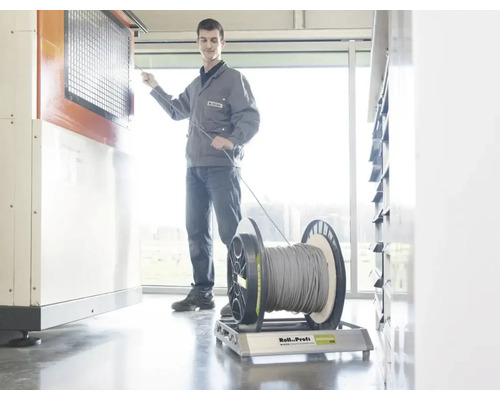 Un artisan tire un câble d'un touret sur un dérouleur Roll Profi Original dans un atelier lumineux.
