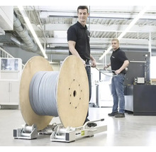 Deux hommes dans un atelier lumineux manipulent un grand touret de câble sur un support de déroulage métallique Roll-Profi.