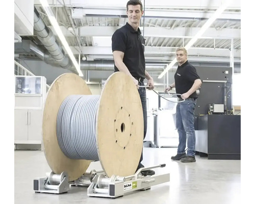 Deux hommes dans un atelier lumineux manipulent un grand touret de câble sur un support de déroulage métallique Roll-Profi.