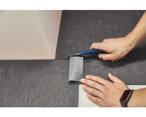 Zuschneiden von dunklem Vlies mit einem Cuttermesser an einer Wandecke.