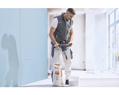 Artisan mélangeant de l'enduit dans un seau avec un malaxeur électrique à côté d'un sac de Knauf Allround.