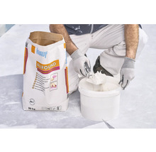 Un artisan prélève de l'enduit dans un seau à côté d'un sac de 20 kilogrammes d'enduit universel Knauf Allround 2 en 1.