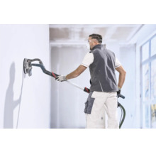 Un artisan lisse un mur avec une ponceuse girafe dans une pièce intérieure lumineuse.