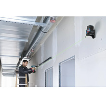 Un artisan utilise un laser en croix Bosch avec faisceau vert pour aligner un rail sur une cloison sèche avec une perceuse.