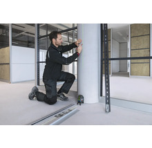 Un artisan utilise un laser à lignes croisées Bosch pour projeter une ligne laser verte verticale sur un pilier en béton pour le marquage.