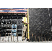 Ouvrier utilisant un long niveau à bulle sur un mur de coffrage sur un chantier avec échafaudage et acier d'armature.