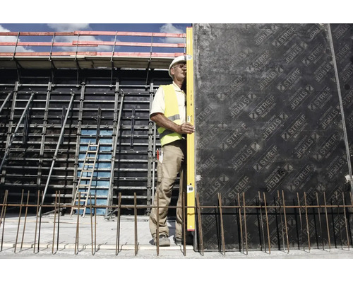 Ouvrier utilisant un long niveau à bulle sur un mur de coffrage sur un chantier avec échafaudage et acier d'armature.