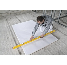Artisan découpant une plaque de plâtre avec un cutter et un niveau à bulle sur un chantier de construction.